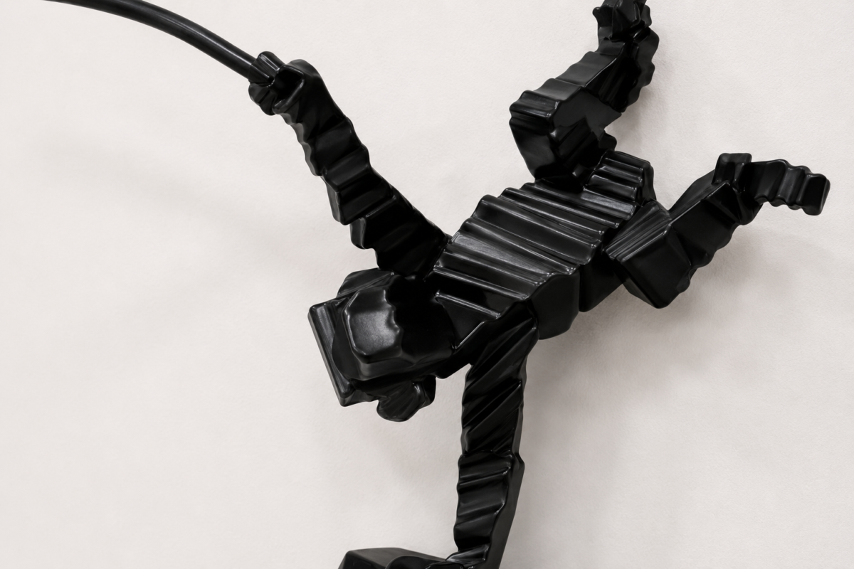 Abstract black sculpture composed of glossy, segmented tubes arranged to resemble a dynamic, dancing figure against a pale background.